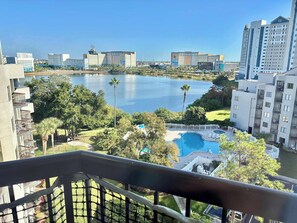 A view from a balcony overlooking a lake, with a pool and greenery in the foreground, and high-rise buildings in the background. - 1802 Enclave-2-m (Orlando)
