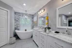 A modern bathroom with a freestanding bathtub, two sinks, and a large mirror. - 1331 Normandy Cir (Palm Harbor)