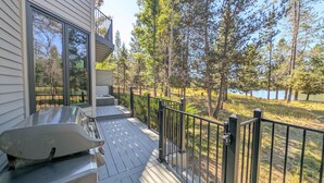 A wooden deck with a hot tub, a metal railing, and a view of a lake surrounded by trees. - 12 Siskin (Bend)