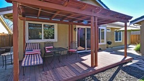 Un patio couvert avec une pergola, des sièges d’extérieur et un barbecue.