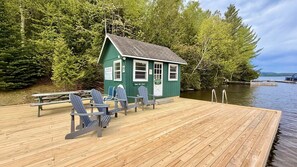 Une petite cabane verte avec un quai qui s’avance sur un lac, le tout entouré d’arbres.