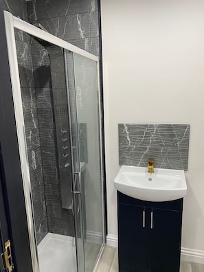 A modern bathroom with a glass shower enclosure, a white sink with a gold faucet, and dark cabinets. - Great Place in Northwood (Northwood)