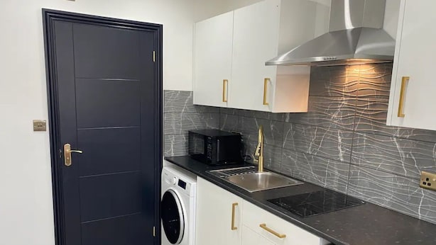 Una cocina compacta con lavadora, microondas y extractor de acero inoxidable.