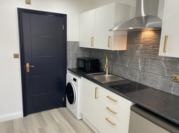 A compact kitchen with a washing machine, a microwave, and a stainless steel range hood. - Great Place in Northwood (Northwood)