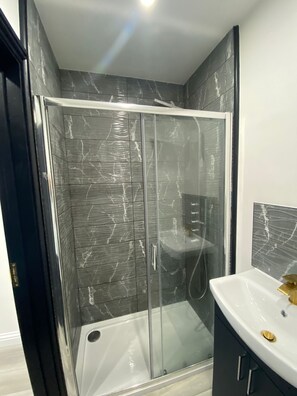 A modern bathroom with a glass-enclosed shower, a white sink with gold fixtures, and marble-patterned walls. - Great Place in Northwood (Northwood)