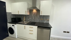 Cocina compacta con armarios blancos, lavavajillas de acero inoxidable, lavadora y encimera negra.