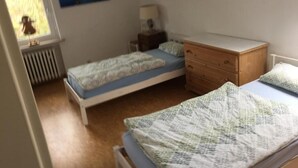 A bedroom with two single beds, a wooden dresser, a nightstand, a window with a view, and a radiator.