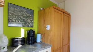 A kitchen with a toaster, coffee maker, and kettle on the counter, a wooden cabinet, and a cityscape painting on the wall.