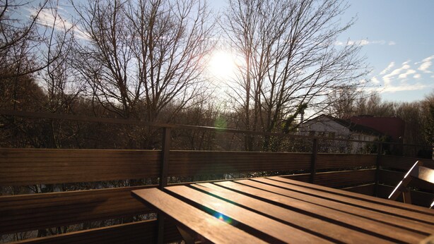 A wooden bench with a metal frame, positioned outdoors with a view of leafless trees and a building in the background.