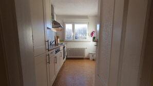 A narrow kitchen with white cabinets, a stove, and a window with a view of trees.
