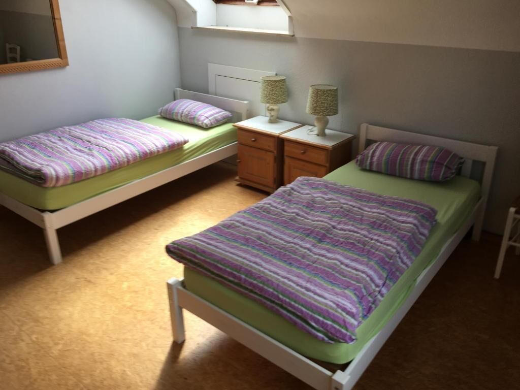 Una camera da letto con due letti singoli, ciascuno con copriletto e cuscino a righe. Sono presenti comodini con lampade e una finestra sopra i letti.