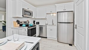 A modern kitchen with white cabinets, stainless steel appliances, and a dining area with a table set for two. - Walk to Beach & Boardwalk • Pool • Family Suite Sleeps 8 • Full Kitchen (Myrtle Beach)
