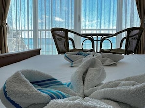 Een hotelkamer met een bed, twee stoelen en een groot raam met uitzicht op zee.
