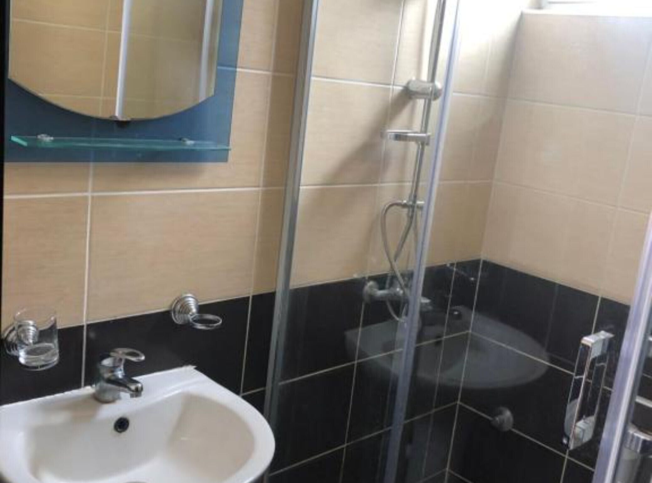 Ein Badezimmer mit einer Duschkabine, einem weißen Waschbecken und einem Spiegel darüber.