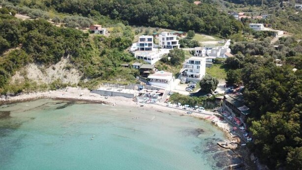 An aerial view of a coastal area with a small boat in the water, surrounded by buildings and greenery. - Casa Mila Bungalows - Family Bungalow (Ulcinj)