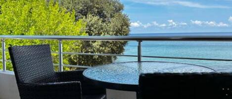 Een balkon met een ronde tafel en twee stoelen, met uitzicht op water en groen.