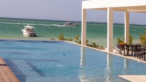 Une piscine à débordement offrant une vue sur l’océan et un bateau.