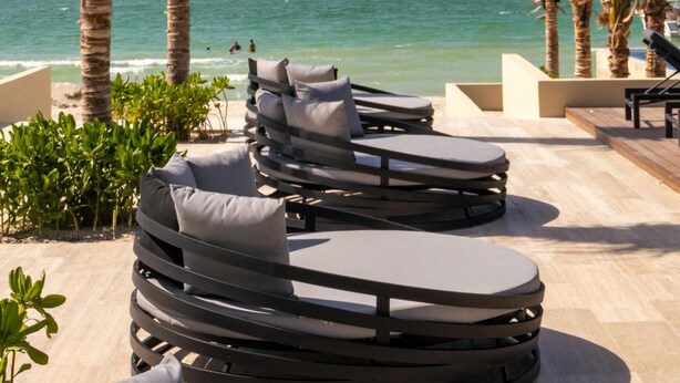 Un espace de détente aménagé sur la plage, avec des chaises longues et des palmiers, offrant une vue sur la mer.