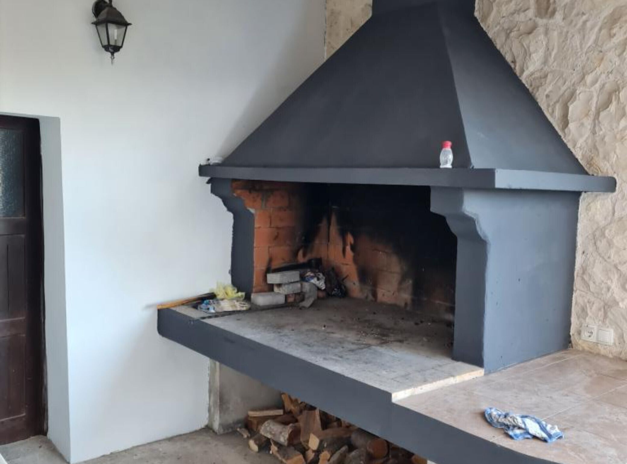 Un camino in pietra con una mensola nera, una piccola bottiglia in cima e un fuoco acceso all'interno.