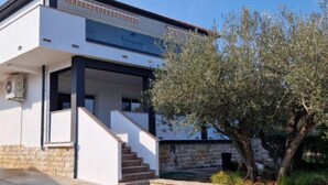 A modern two-story building with a stone base and a white upper level. There is a staircase leading to the upper floor, and a tree is visible in the foreground. - Apartments Nena - Studio apartment (Ugljan)