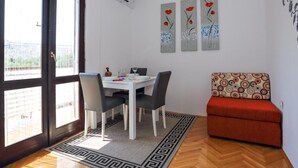 A dining area with a white table and chairs, a patterned rug, and a sofa with a circular cushion. - Apartments Nena - Studio apartment (Ugljan)