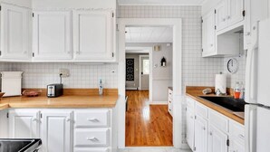 A modern kitchen with white cabinetry, a wooden countertop, and a view into the dining area. - Saratoga Track House, Pet Friendly, Workspace (Saratoga Springs)