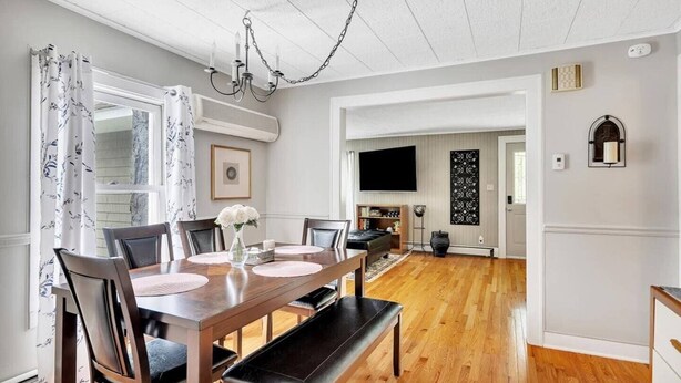 A dining area with a wooden table, chairs, and a bench. There is a chandelier, a flat-screen TV, and a decorative wall piece. - Saratoga Track House, Pet Friendly, Workspace (Saratoga Springs)