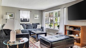 A modern living room with a sofa, ottoman, coffee table, and a flat-screen TV. - Saratoga Track House, Pet Friendly, Workspace (Saratoga Springs)