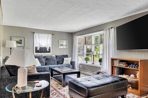 Ein modernes Wohnzimmer mit Sofa, Pouf, Couchtisch und einem Flachbildfernseher.