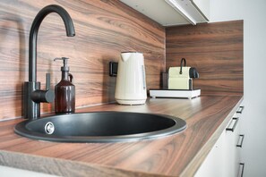 Eine moderne Küche mit einem schwarzen Spülbecken, einer Kaffeemaschine und einem Wasserkocher auf der Arbeitsplatte.