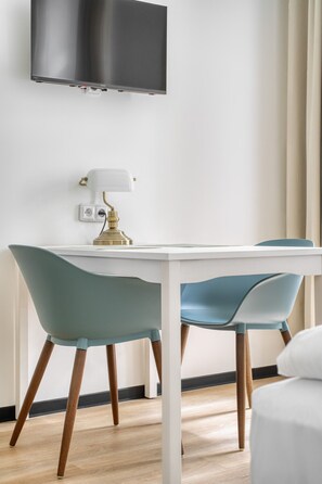 Ein moderner Essbereich mit einem weißen Tisch, blaugrünen Stühlen, einer goldenen Lampe und einem an der Wand befestigten Fernseher.