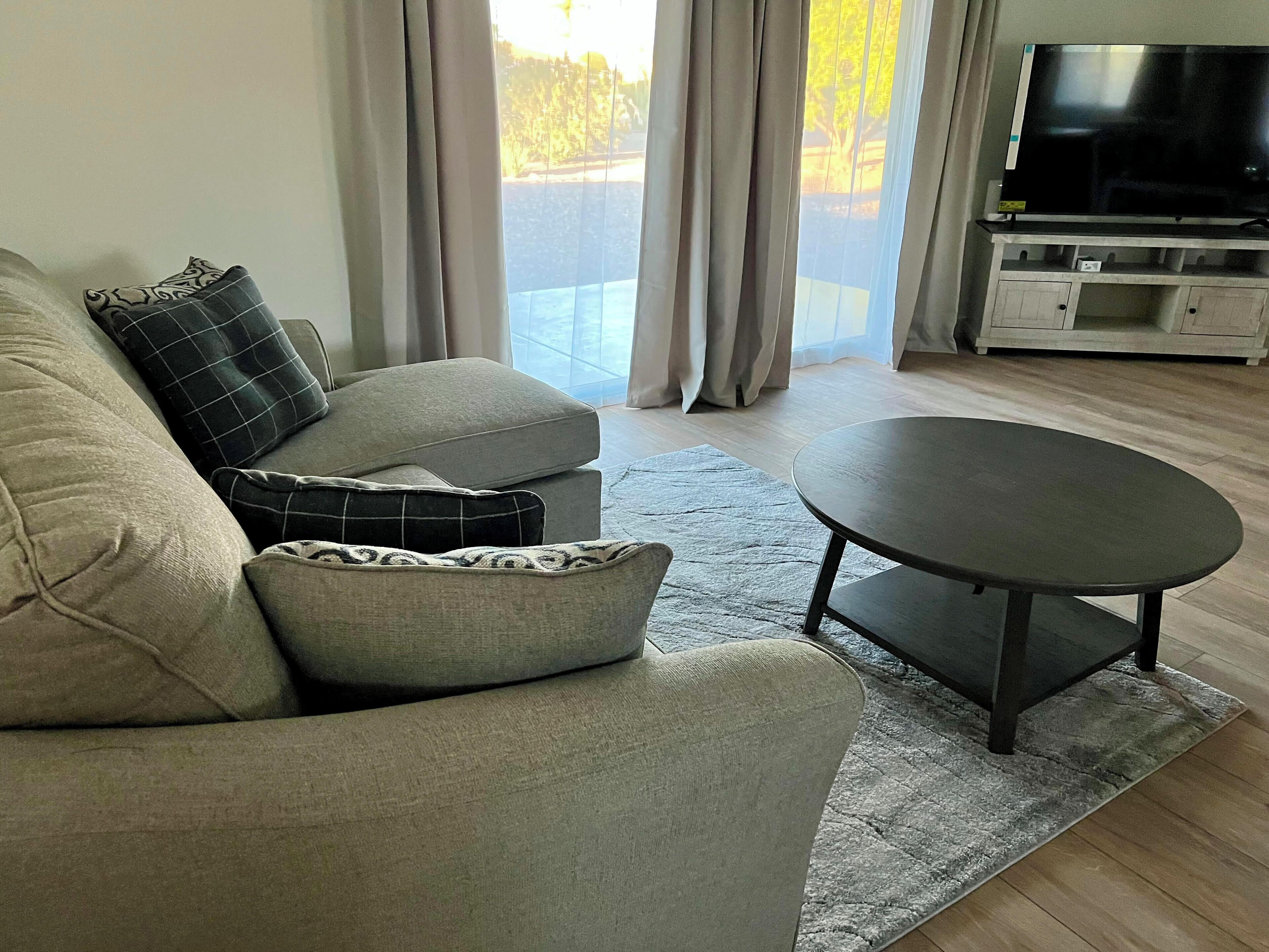 A modern living room with a grey sofa, a round coffee table, and a flat-screen TV on a stand.