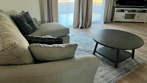 A modern living room with a grey sofa, a round coffee table, and a flat-screen TV on a stand.