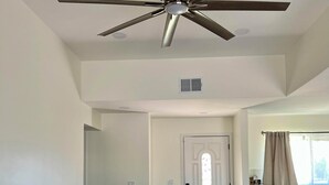 A dining room with a wooden table, white chairs, and a ceiling fan.