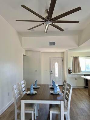 A dining room with a wooden table, white chairs, and a ceiling fan.
