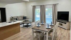 A modern living room with a sofa, a dining table with chairs, a TV, and a ceiling fan.