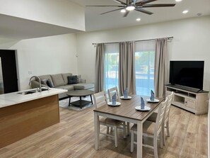 A modern living room with a sofa, a dining table with chairs, a TV, and a ceiling fan.