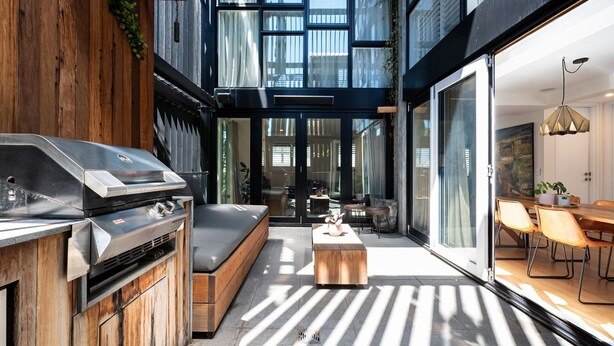 Un patio exterior moderno con una parrilla empotrada, zona de estar y comedor con sillas y una mesa.