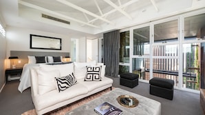 Una habitación de hotel moderna con una cama, un sofá, una mesa de centro y un amplio ventanal corredera que da a un balcón exterior.