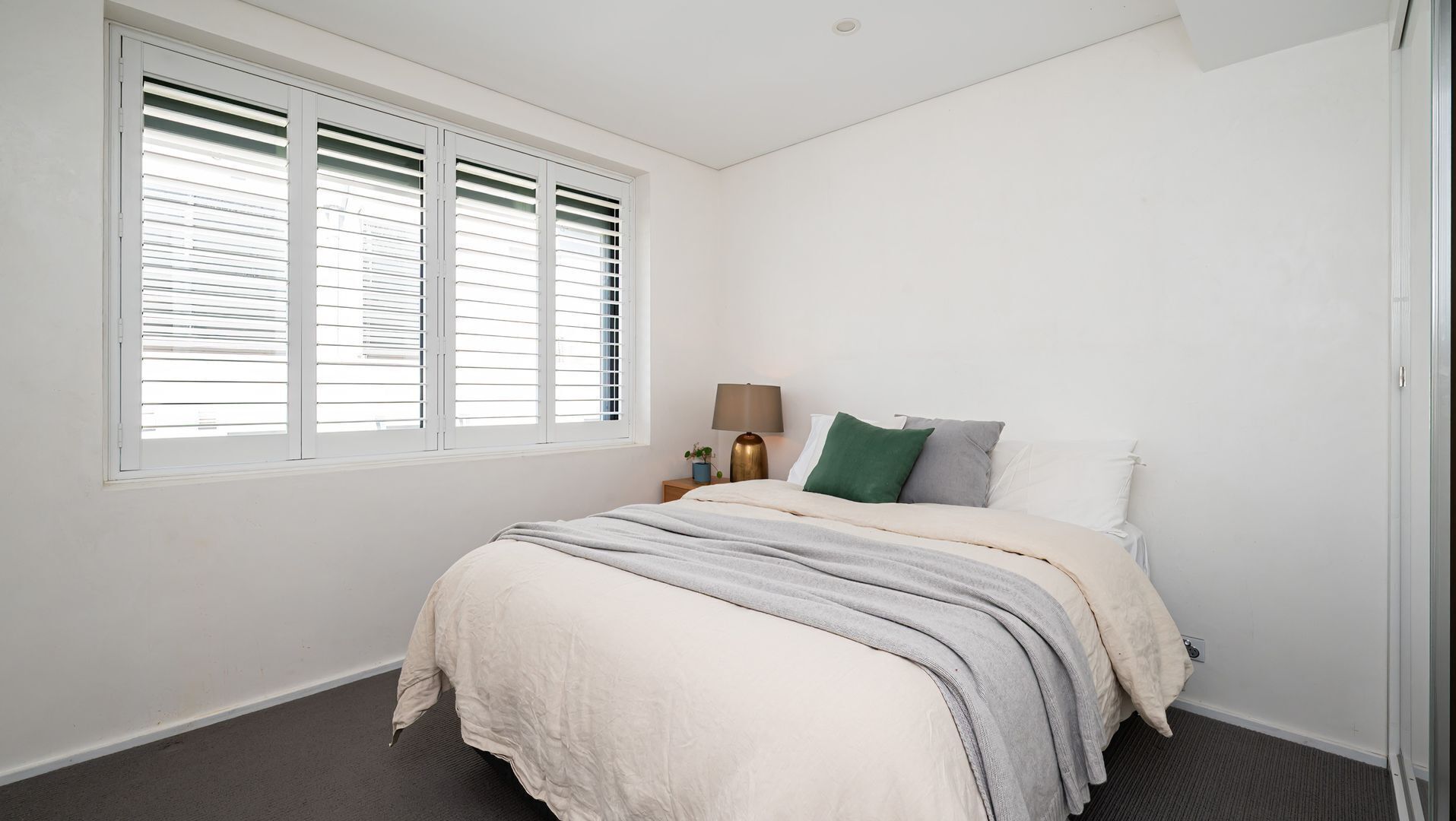A bedroom with a bed, a nightstand, a lamp, and a window with blinds.