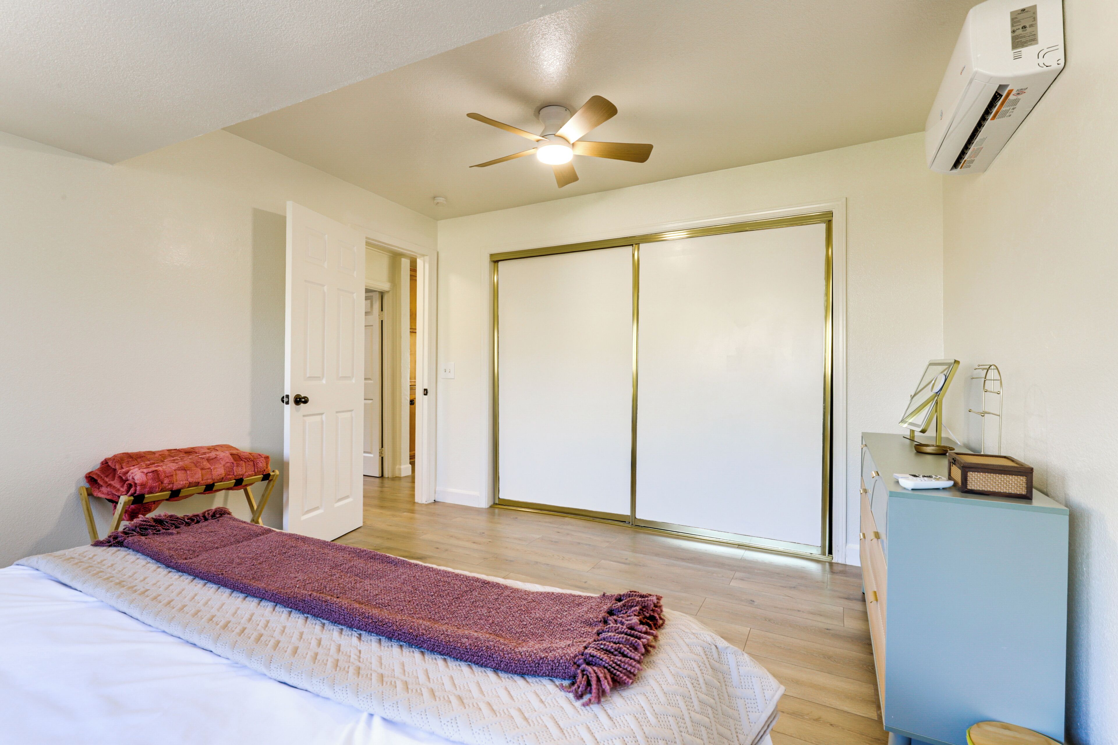 A bedroom with a bed, a ceiling fan, a wardrobe, and a desk with a lamp.