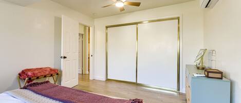A bedroom with a bed, a ceiling fan, a wardrobe, and a desk with a lamp.