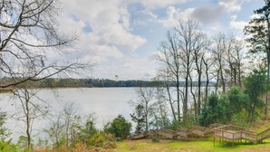 A lakeside view with wooden deck chairs and a water tower in the distance. - Private Dock & Hot Tub: Lakefront Eufaula Escape (Eufaula)