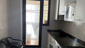 Cucina moderna con mobili bianchi, piano di lavoro in acciaio inossidabile e forno a microonde integrato. Si nota una sedia nera e un piccolo tavolo di legno.