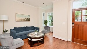 A living room with a blue sofa, a round coffee table, and a gray armchair. - Bright & Spacious 5BR Home Near Capitol Hill • Free Parking (Washington DC)