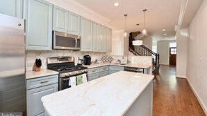 A modern kitchen with light blue cabinets, stainless steel appliances, and a marble island. - Bright & Spacious 5BR Home Near Capitol Hill • Free Parking (Washington DC)