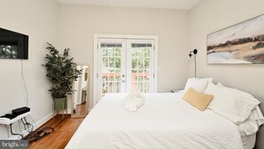 A bedroom with a bed, a potted plant, a mirror, and a painting on the wall. - Bright & Spacious 5BR Home Near Capitol Hill • Free Parking (Washington DC)
