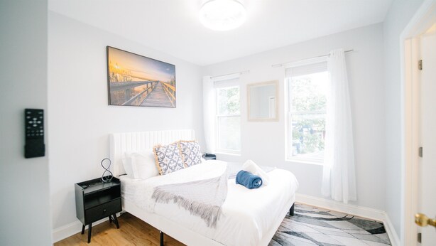 Une chambre à coucher avec un lit, des tables de chevet, un tableau et une fenêtre avec des rideaux.