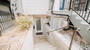 A residential building with a concrete staircase leading to a door, a metal fence, and a small garden area with a bush. - Comfy 1BR Basement DC | Sleeps 5 | Near Metro (Washington DC)