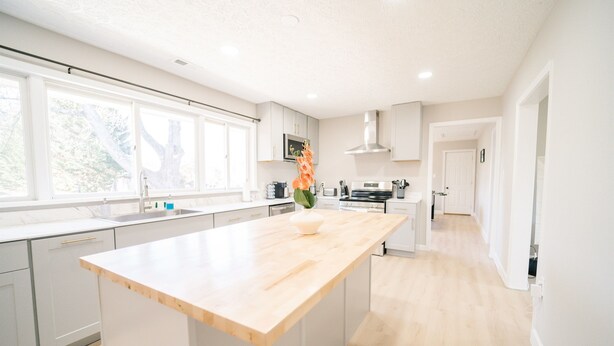 A modern kitchen with white cabinetry, a wooden island, and a view of the outdoors.